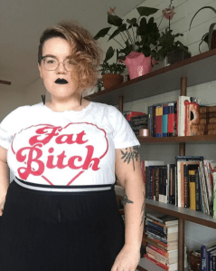 The author wearing black lipstick and a t-shirt saying "Fat Bitch" and looking very stern
